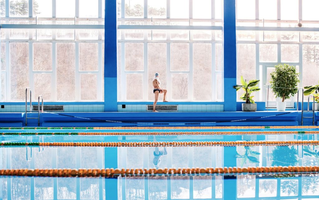 Senior man stretching by the indoor swimming pool.